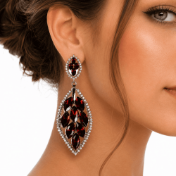 Gros plan sur boucles d’oreilles pendantes grenat à strass portées par une femme élégante sur fond blanc