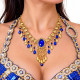 Collier oriental bleu roi et or porté par une danseuse orientale, orné d'une pierre bleue centrale, de motifs floraux dorés et de pendentifs scintillants