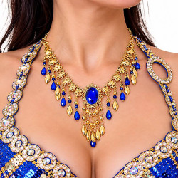 Collier oriental bleu roi et or porté par une danseuse orientale, orné d'une pierre bleue centrale, de motifs floraux dorés et de pendentifs scintillants